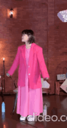 a woman in a pink dress and pink jacket is standing in front of a brick wall ..