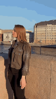 a woman in a jacket with rhinestones on the sleeves stands in front of a river