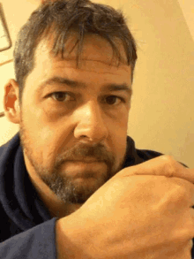 a man with a beard looks at the camera with his hand on his face