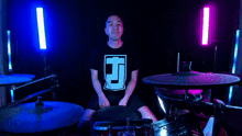a man in a black shirt with the letter j on it is sitting in front of a drum set