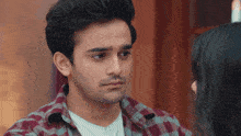 a man in a plaid shirt looks at a woman in a white t-shirt