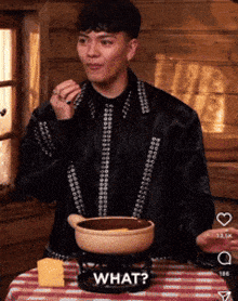 a man is sitting at a table with a pot of food and a sign that says what on it