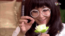 a woman wearing glasses and a wig is holding a green flower in her hand .