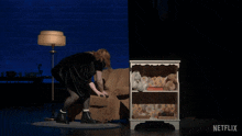 a woman in a black dress is holding a hammer in front of a shelf that says netflix