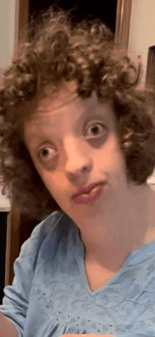 a young girl with curly hair is wearing a blue shirt