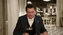 a man in a suit is sitting at a table with a glass of beer in front of him