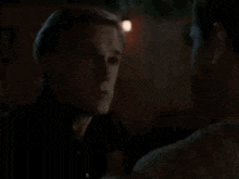 two men are standing next to each other in a dark room looking at each other .
