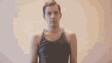 a man in a tank top is standing in front of a white wall and looking at the camera .