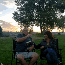 a man and a woman are sitting in chairs in a field talking