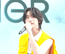 a man in a yellow vest sings into a microphone in front of a sign that says n.e.i.