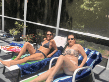 two women in bikinis are laying on lounge chairs on a screened in porch