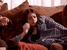 a woman laying on a couch with a blue blanket on her shoulders
