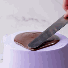 a person spreading chocolate on a purple cake with a spatula