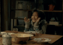 a young girl is sitting at a table with a bowl of food