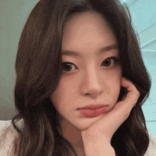 a woman with her hand on her face looks at the camera