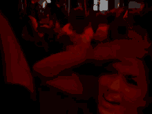 a woman in a red dress is standing in a dark room with a crowd behind her