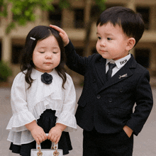 a boy in a dior suit is touching the head of a girl