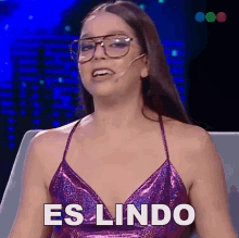 a woman wearing glasses and a purple top has the word es lindo on her chest