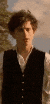 a man in a black vest and white shirt is standing in front of trees .
