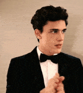 a man in a tuxedo and bow tie is clapping his hands .