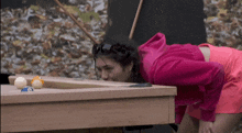a woman in a pink jacket is playing pool on a table