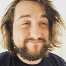 a man with long hair and a beard is smiling for the camera