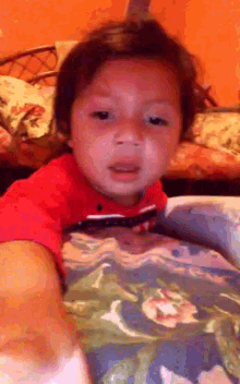 a young boy in a red shirt is sitting on a bed