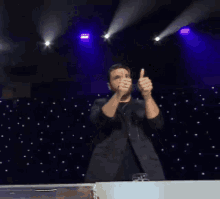 a man in a suit is giving a thumbs up on a stage