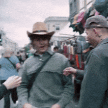 a man in a cowboy hat is talking to another man in a crowded street