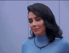 a woman wearing a blue turtleneck sweater is making a funny face