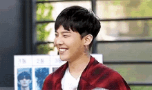a young man wearing a red plaid jacket and a white t-shirt is smiling .