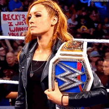 a woman in a leather jacket is holding a wrestling championship belt in front of a crowd .