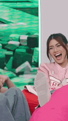 a woman in a pink shirt is laughing while sitting on a pink pillow