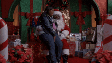 a woman sits on santa 's lap in front of presents