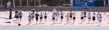 a group of people are running on a beach with a flag that says bakery in the background