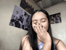 a girl with black nails is covering her mouth with her hand in front of posters on the wall