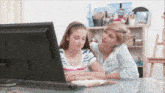 a mother and daughter are looking at a computer screen together