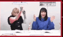 two women are sitting at a table with their hands up .