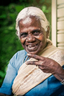 a woman with gray hair and a blue shirt is smiling and making a peace sign