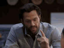 a man with a beard is sitting at a table pointing at something
