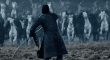 a man is holding a sword in front of a herd of horses in a field .