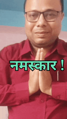 a man wearing glasses and a red shirt has his hands folded in front of him and the words " namaste " written above him