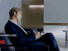 a man in a suit is sitting in a chair writing in a book