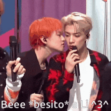 a man with red hair is kissing another man on the cheek while holding microphones .
