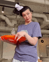a woman in a purple shirt is holding an orange tray with a bottle on it