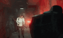 a man in a suit is standing in a dark hallway with a red light coming from the ceiling .
