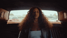 a woman sitting in the back seat of a car wearing a white top with the letter w on it