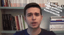 a man is standing in front of a bookshelf with a stack of books on it .