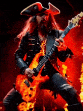 a man with long hair and a beard is playing a guitar in a pirate hat .