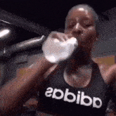 a woman wearing an adidas tank top is drinking water from a bottle